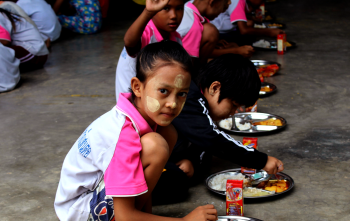 Ein junges Mädchen setzt sich hin, um ihr Essen in der Schule in Thailand zu essen.