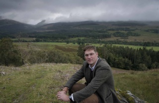 Magnus MacFarlane-Barrow nimmt auf einem Hügel in den Highlands von Schottland Platz.