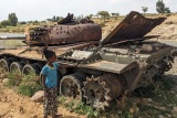 Image of a child standing next to an abandoned tank by the roadside.
