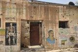 Image of a wall with murals drawn on and bullet holes left after the recent conflict.