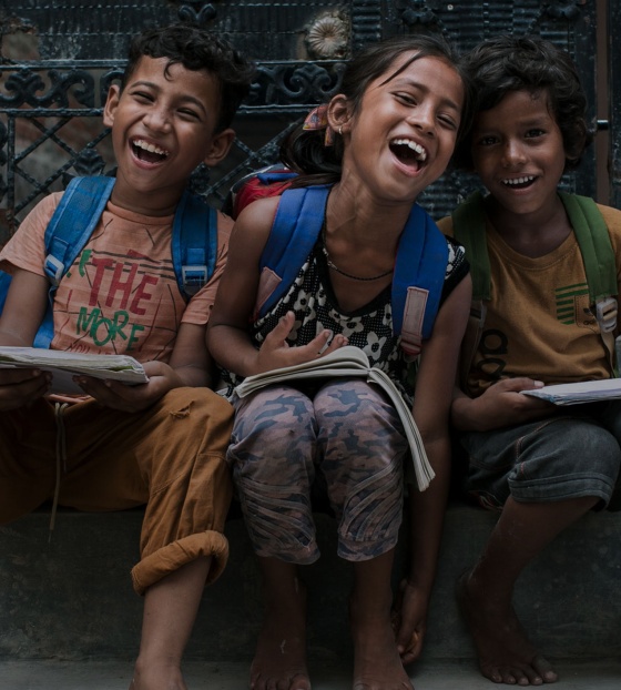 Three children sitting on some steps laughing and smiling looking towards the camera.