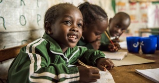 Ein junger Junge lächelt, während er im Unterricht in Kenia Notizen macht.