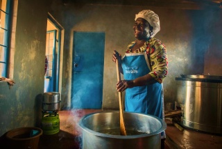 Eine ehrenamtliche Köchin lacht, während sie in Malawi Essen zubereitet.