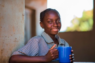 Ein junges Mädchen mit einer Tasse Porridge in Sambia.