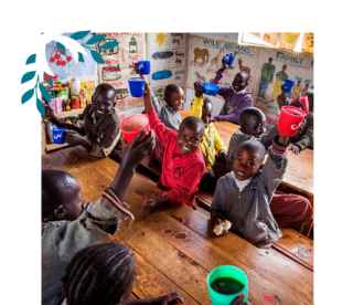 Children sitting in a classroom raising their mugs up